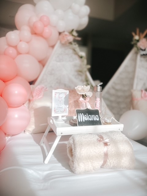 A boho-inspired sleepover setup featuring a light pink teepee adorned with a pastel balloon garland, a personalized name plate, and a matching water bottle. The cozy scene is completed with plush pillows, blankets, and delicate accents.