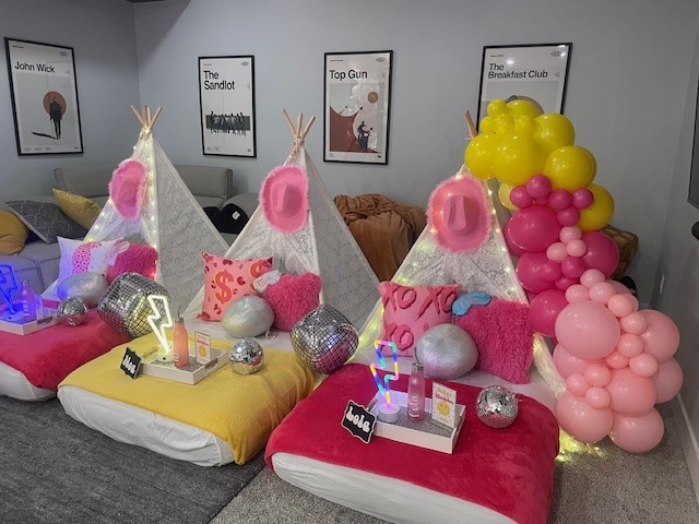 A Preppy Disco Cowgirl-themed sleepover setup featuring pink and white teepees, disco balls, cowgirl hats, and pastel decor. The scene is accented with shimmering string lights and a stylish picnic table setup, creating a fun and glamorous vibe.