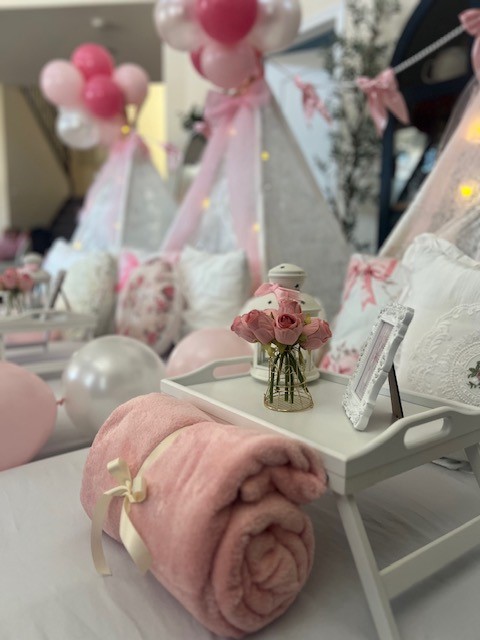 A wide view of a LoveShackFancy-inspired sleepover setup featuring multiple floral-print teepees arranged in a cozy layout. The scene includes pastel pillows, soft blankets, lace accents, and twinkling string lights, creating a luxurious and inviting atmosphere.