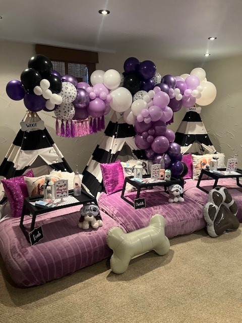 A Let’s Pawty-themed sleepover setup featuring paw-print pillows, pastel teepees, and adorable dog-themed decor. The scene is complete with plush blankets, string lights, and fun accents like dog bowls and faux bone treats, creating a playful and cozy atmosphere.