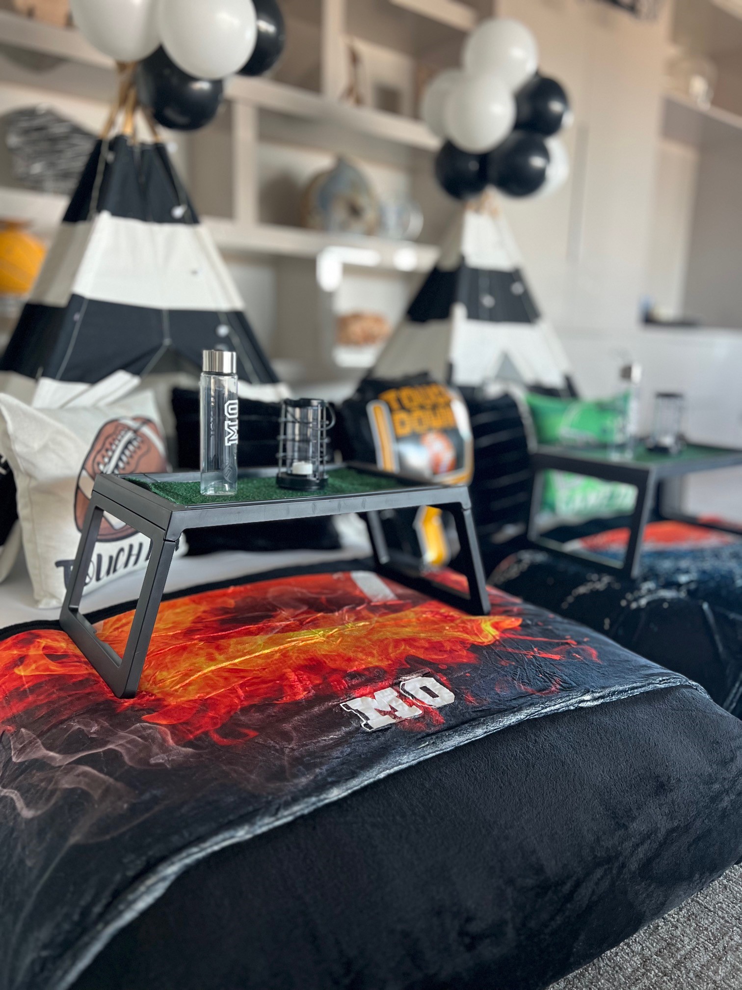 Close-up of a football-themed sleepover setup with personalized football blankets, custom water bottles, and decorative mylar football balloons.